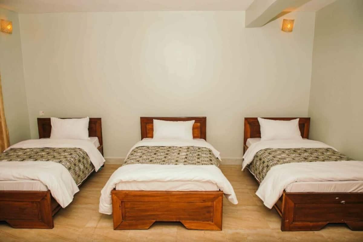 Habitación de hotel con tres camas de madera dispuestas en fila, cada una con almohada blanca y cubrecama estampado.