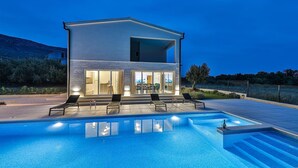 Een modern huis met twee verdiepingen en een zwembad ervoor.