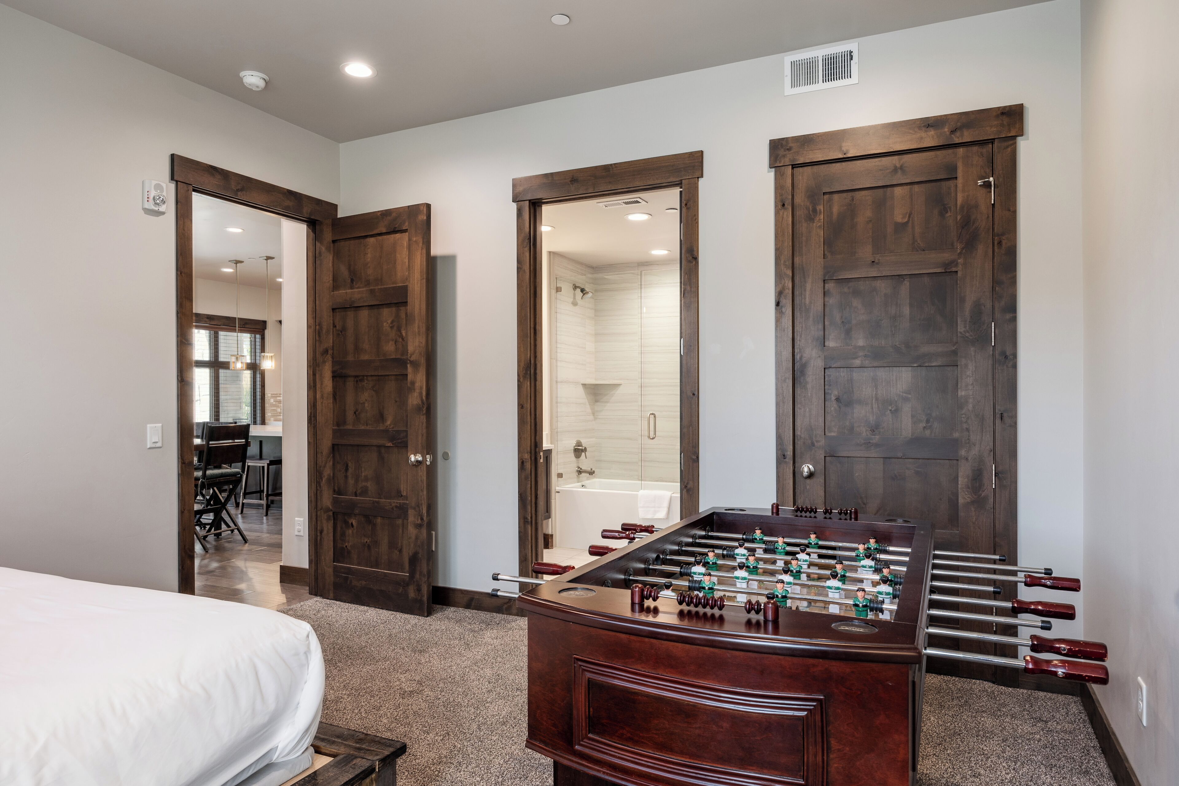 Una habitación con cama, mesa de fútbol de mesa y puertas de madera que dan a un baño y otra habitación.