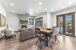 Un salón espacioso con chimenea, un comedor con mesa y sillas de madera, y grandes ventanales con vistas al exterior.
