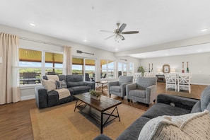 A spacious living room with a large window, a ceiling fan, and a dining area with white furniture. - Private Indoor Pool! Sleeps 35 + Lake View! (Kimberling City)
