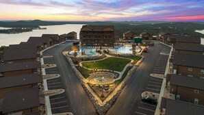A hotel with a central courtyard, multiple swimming pools, and a view of a river at sunset.