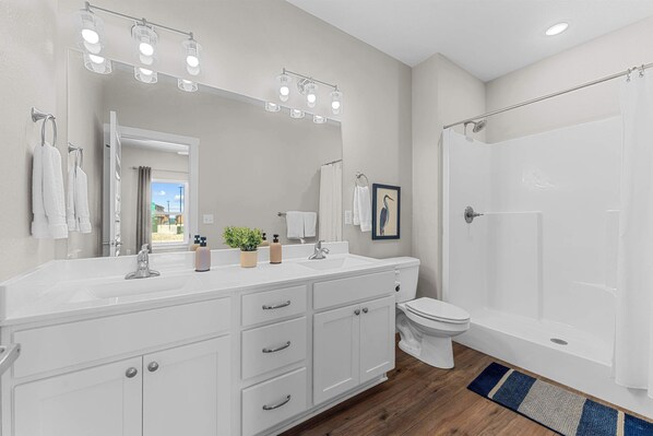 A modern bathroom with a white vanity, a large mirror, a shower, and a view of the outdoors.