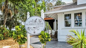 A sign for The Hibiscus House of Fort Myers with a white building in the background. - Hibiscus House Bed & Breakfast Inn Flamingo Suite (Fort Myers)