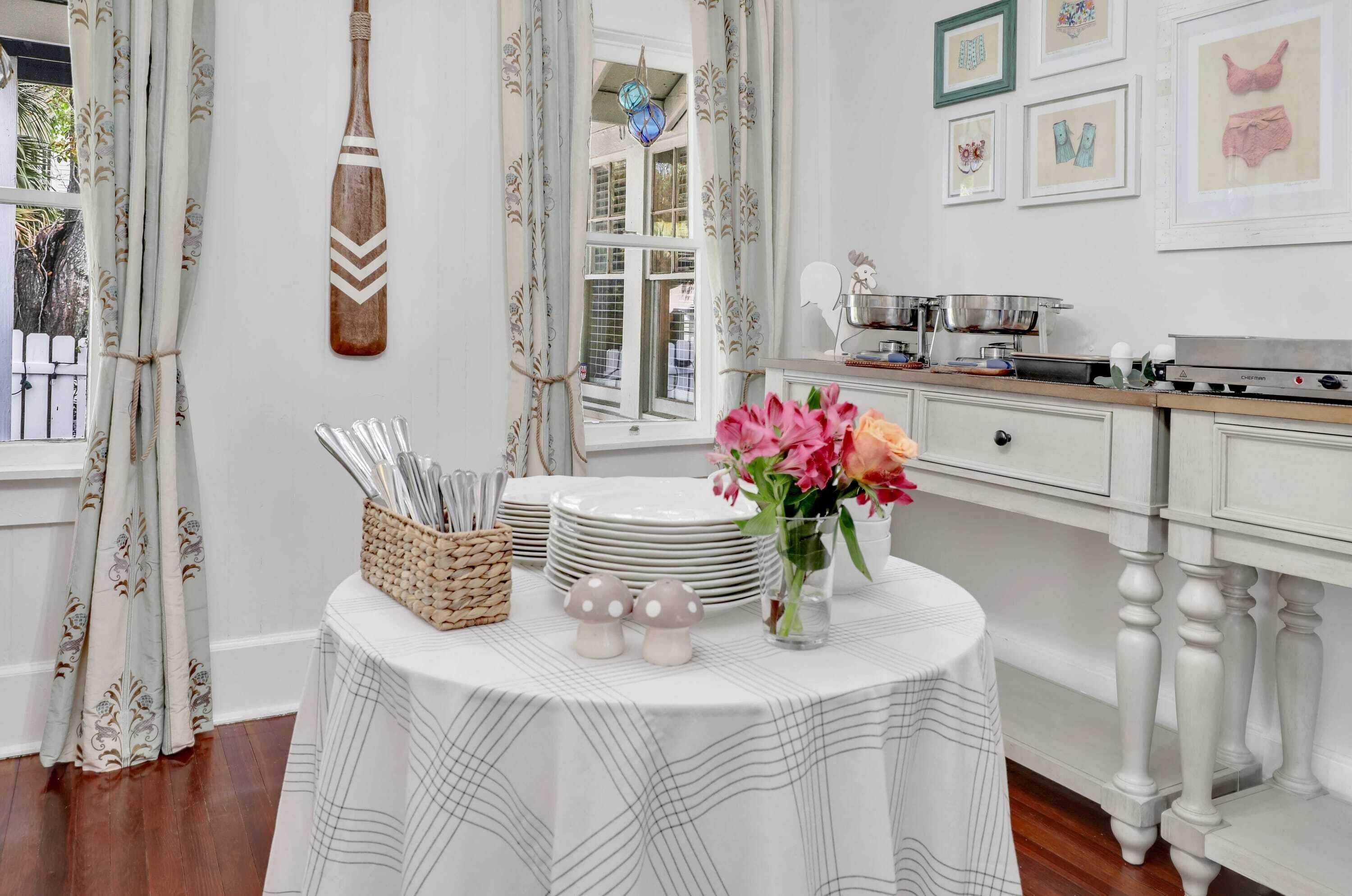 A dining area with a table set for four, a decorative wall hanging, and a window with curtains.