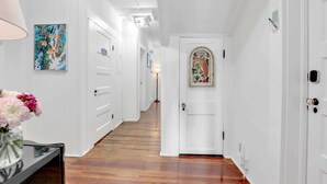 Um corredor com paredes brancas, piso de madeira, uma porta com arco decorativo e uma obra de arte emoldurada na parede.