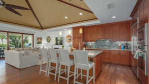 A spacious kitchen with wooden cabinets, a large island, and a dining area with white furniture. - Luxury + Privacy ✨ Near Putting Green ⛳ Beach Club Access 🏖️ (Waimea)