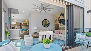 Ein modernes Wohnzimmer mit einem blauen runden Tisch, einer Couch und einem großen Fenster mit Blick auf einen Pool.