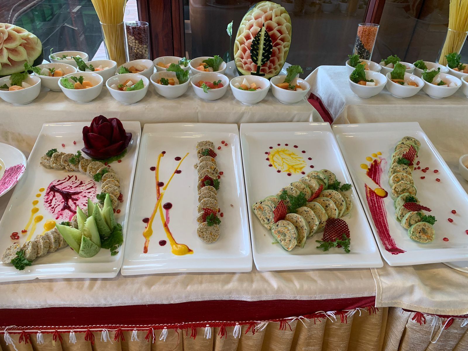 A table with various dishes, including a watermelon carved into a leaf, and several plated appetizers with garnishes.
