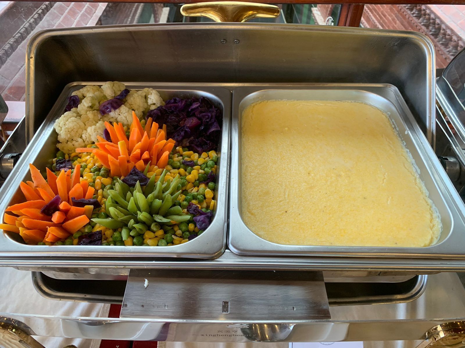 A buffet with two trays: one with assorted vegetables and another with a yellow creamy dish.