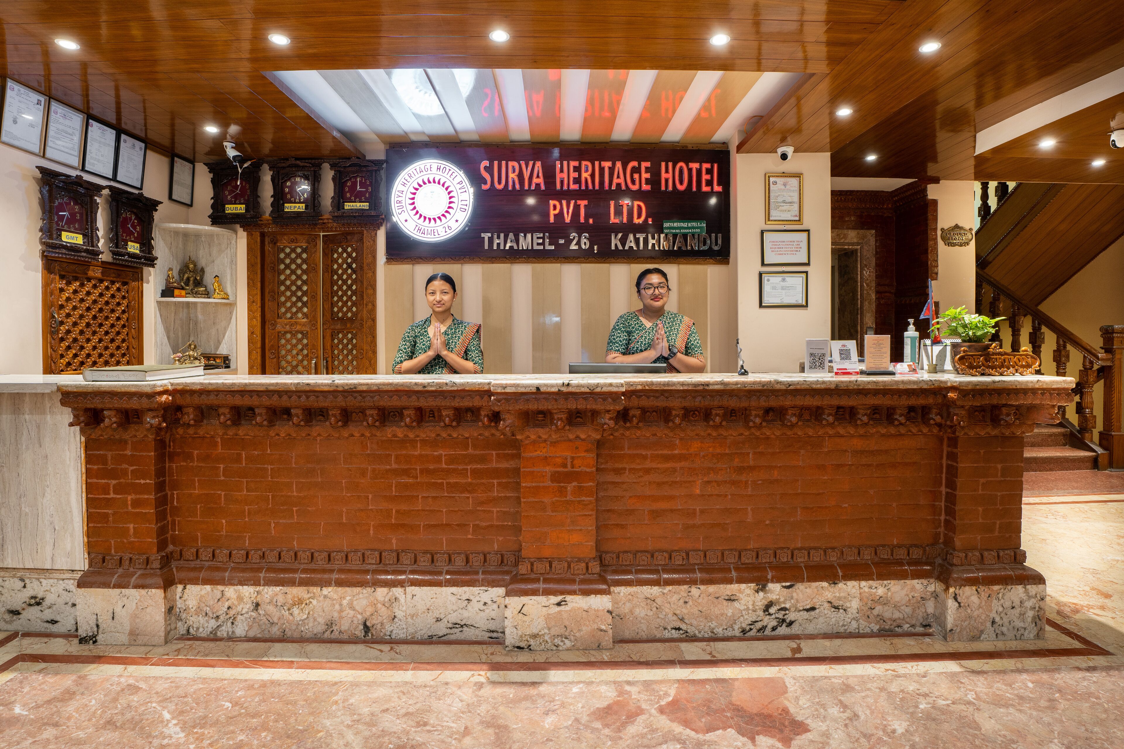 A reception desk at Surya Heritage Hotel Pvt. Ltd. with two staff members behind it, a signboard above, and traditional Nepalese decor.
