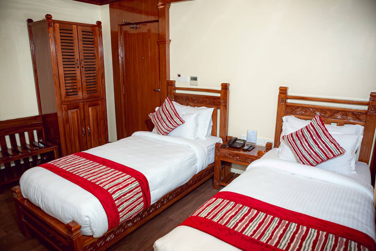 A hotel room with two wooden beds, each with a red and white striped bedspread and matching pillows. There is a wooden wardrobe and a nightstand with a phone and a lamp.