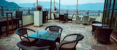 A terrace with wicker furniture, a glass table, and potted plants.