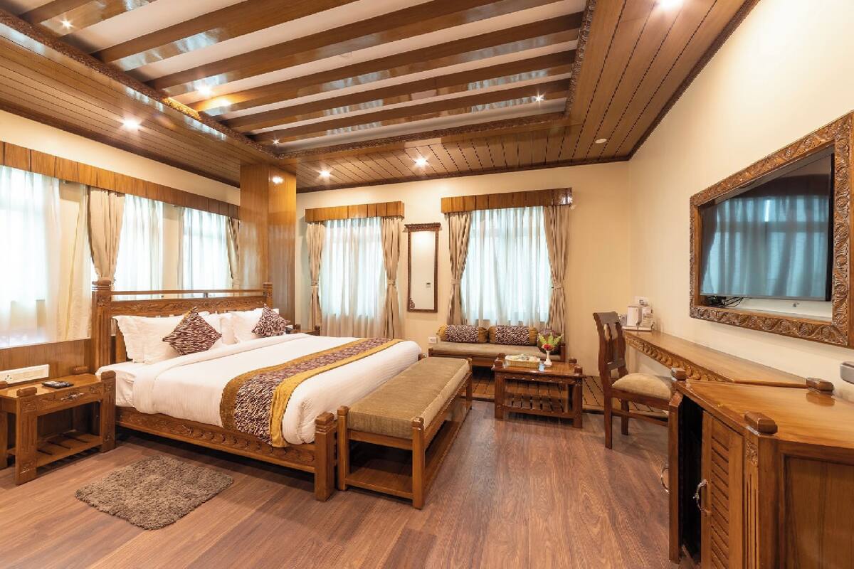 A spacious bedroom with a large bed, wooden furniture, and a television on the wall.