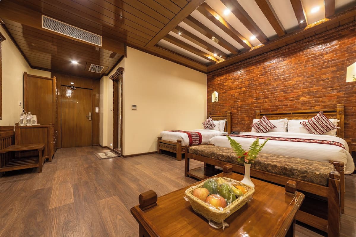 A hotel room with a wooden floor, a brick wall, a bed with white bedding, a wooden bench, and a table with a fruit basket.