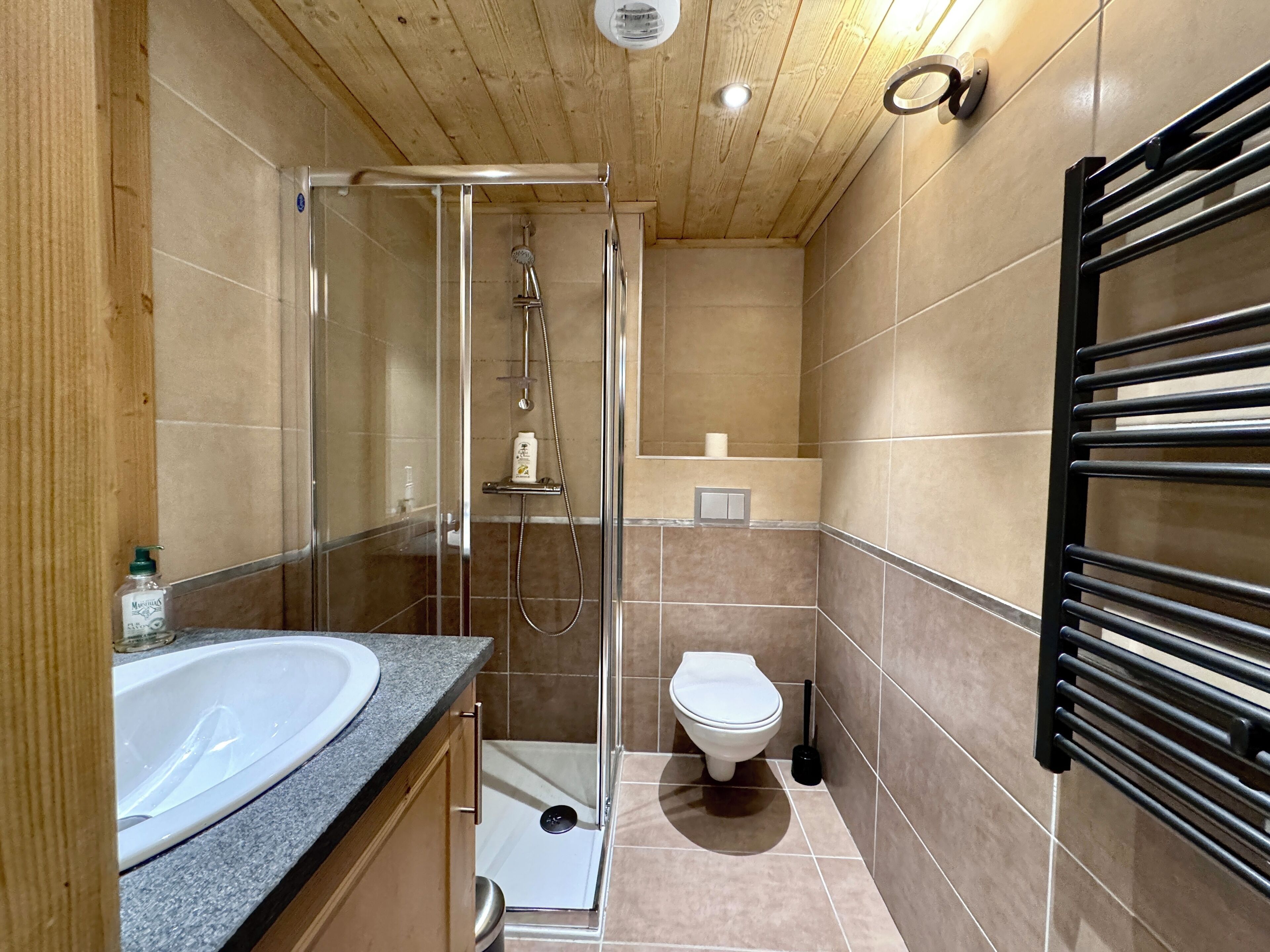 Et moderne badeværelse med et glasafskærmet brusebad, en hvid vask og et toilet.
