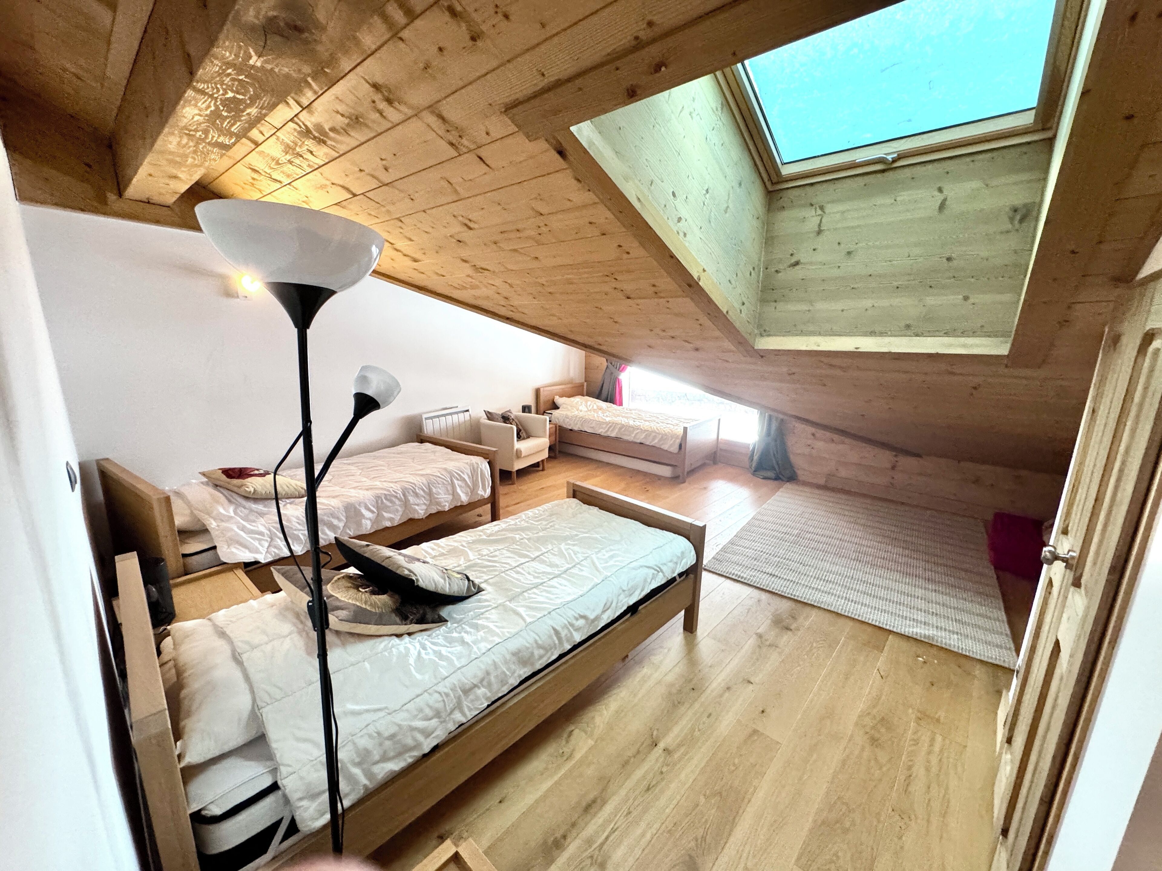 A cozy attic bedroom with a skylight, wooden beams, and a bed with a lamp.