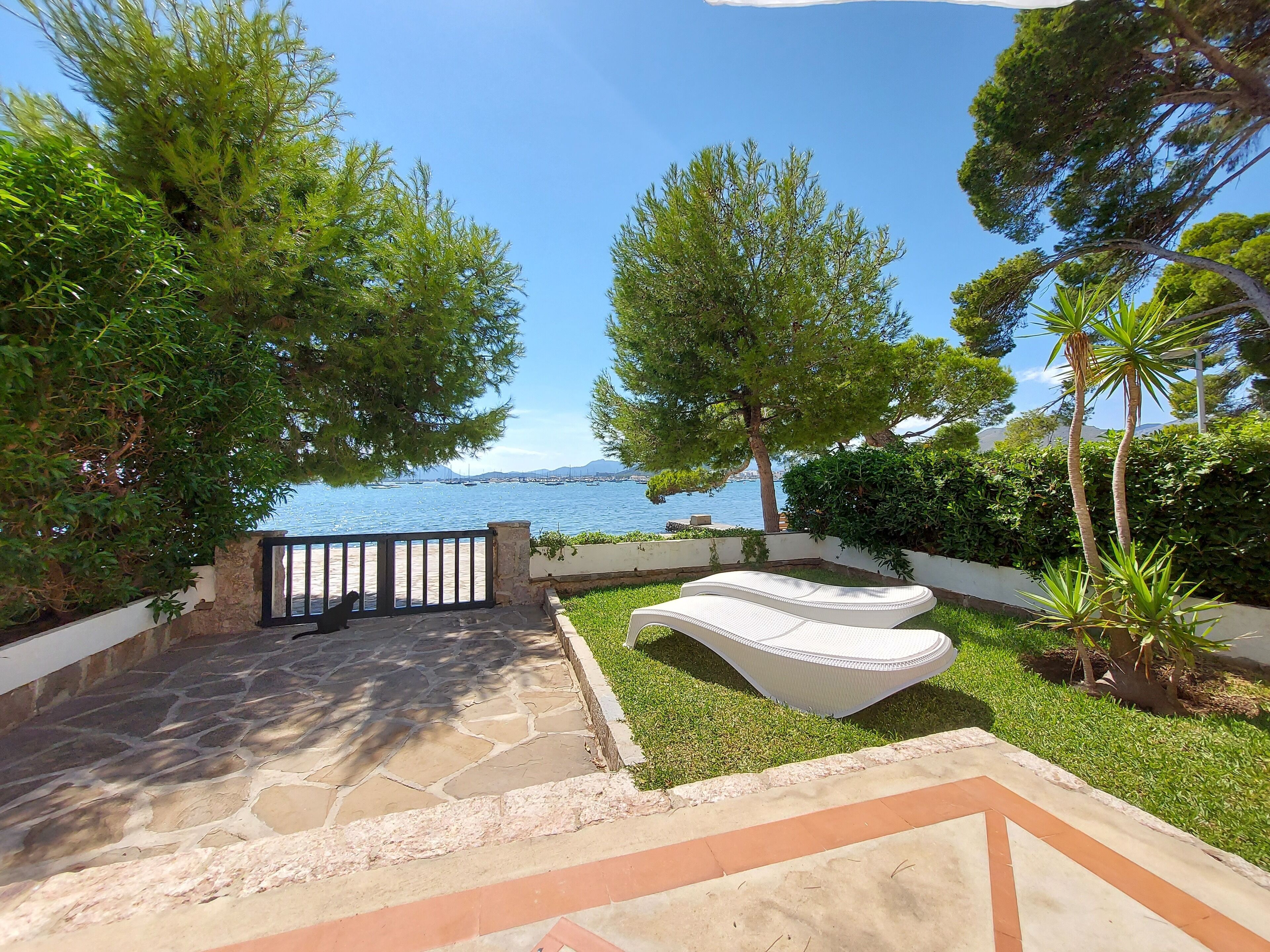 Une terrasse dallée de pierres, avec un banc blanc, entourée de verdure et offrant une vue sur la mer.