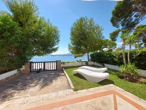 Une terrasse dallée de pierres, avec un banc blanc, entourée de verdure et offrant une vue sur la mer.