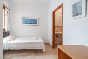 A small, clean room with a bed, a wooden door, a framed picture on the wall, and a small table. - Casa Faro Spacious Pine Walk Property, Covered Terrace, Sea Views.wifi & Air Con (Port de Pollença)