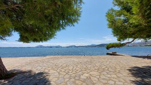 A stone-paved beach with a clear view of the sea and sailboats in the distance.
