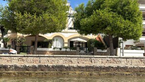 A waterfront hotel with a stone facade, outdoor seating, and a clear view of the water.