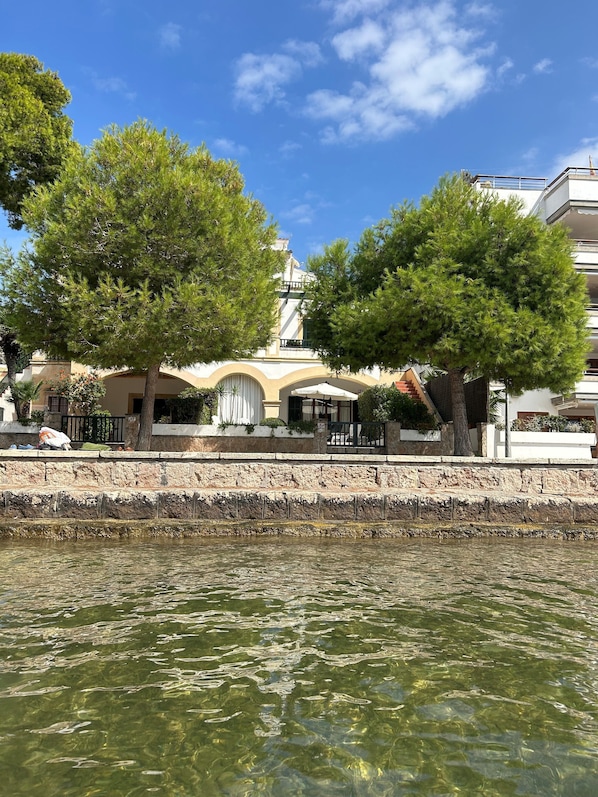 A waterfront hotel with a stone facade, outdoor seating, and a clear view of the water.