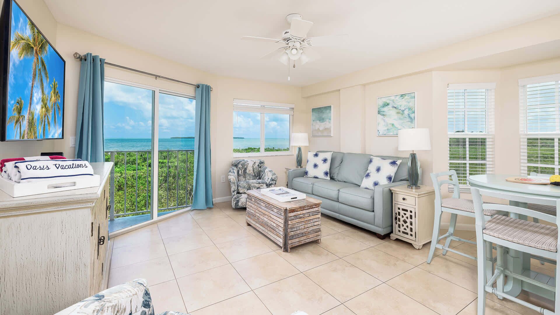 A spacious living area with a balcony overlooking the sea, a sofa, a coffee table, and a dining table.