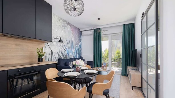 A modern kitchen with dark cabinetry, a dining area with wooden chairs, and a large window with curtains.