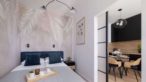 A modern bedroom with a large bed, bedside tables, a small desk, and a dining area with chairs and a table.