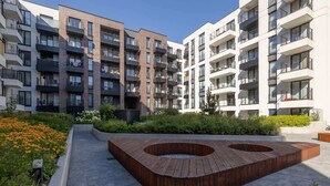 A modern apartment complex with multiple balconies, a central wooden seating area, and a landscaped garden.