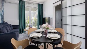 A modern living room with a dark sofa, a dining table set for four, and a sliding glass door.
