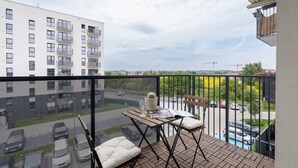A balcony with a table, chairs, and a view of a parking lot and buildings.