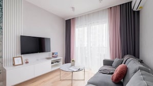A modern living room with a flat-screen TV, a white console, a round coffee table, and a grey sofa.