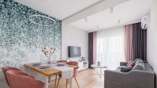 A modern living room with a dining area, a grey sofa, a TV, and a wall with a floral pattern.