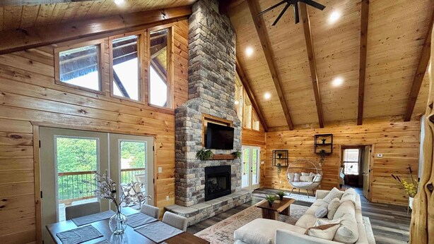 A spacious cabin interior with a stone fireplace, wooden walls, a dining area, and a cozy seating area. - Southern Smoke | Scenic Decks | Hot Tub | Wi-Fi (Rogers)
