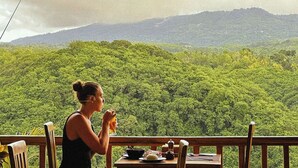A dining area with a table set for two, overlooking a dense forest and a mountain range. - Green Coco Suite (Penida Island)