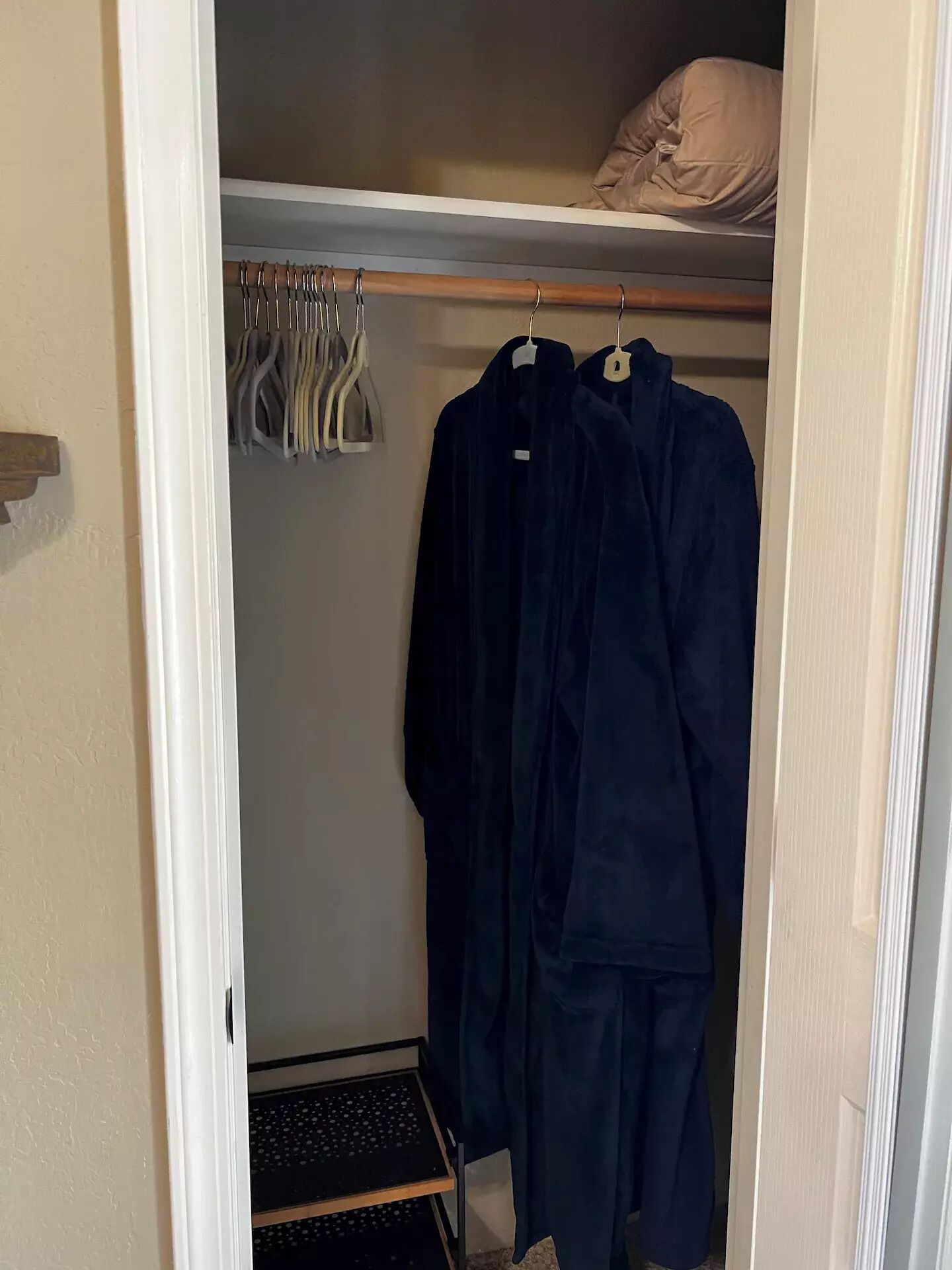 Een inloopkast met kleding en een plank.