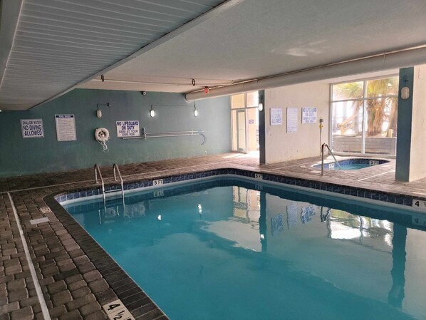 An indoor swimming pool with clear water, marked depth lines, and safety signs on the walls. - Garden City Beach Oceanfront Condo 911 | Rising Tides Properties (Murrells Inlet)
