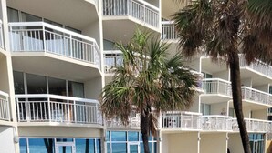 Zona de piscina con vista despejada al océano, rodeada por un edificio de varios pisos con balcones.