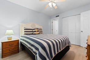 Un dormitorio con cama, mesita de noche, lámpara, ventilador de techo y armario.
