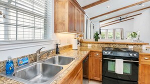 A modern kitchen with granite countertops, stainless steel sinks, wooden cabinets, a black stove, and a window with blinds.