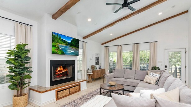 A living room with a fireplace, a sofa, a television, and a large window with curtains.