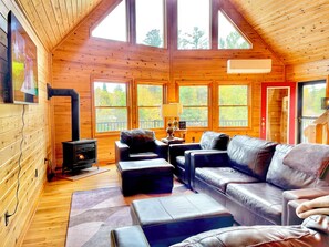 A cozy cabin interior with a fireplace, leather furniture, and large windows.