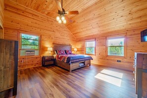 A wooden cabin bedroom with a bed, two bedside tables, a nightstand, a ceiling fan, and windows. - Adirondack Luxury Near Whiteface, Lake Placid (Jay)