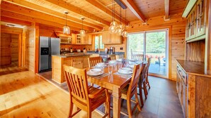 A wooden cabin interior with a dining area, kitchen, and large windows. - Adirondack Luxury Near Whiteface, Lake Placid (Jay)