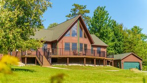 A large, two-story log cabin with a prominent gable roof, a covered porch with chairs, and a garage. - Adirondack Luxury Near Whiteface, Lake Placid (Jay)