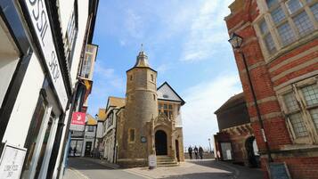 A cobblestone street with historic buildings, including a tower with a pointed roof and a brick building with arched windows.