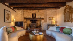 A cozy living room with two white sofas, a round coffee table, a fireplace, and a stone wall.