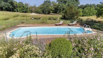 Ein rechteckiger Swimmingpool mit einem Zaun aus Maschendraht, umgeben von einer Rasenfläche mit mehreren Liegestühlen.